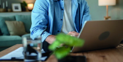 Mann sitzt am Esstisch zuhause und arbeitet am Laptop.