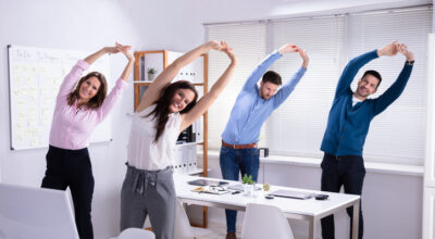 Glückliche Geschäftsleute, die Stretching-Übungen hinter dem Schreibtisch am Arbeitsplatz machen