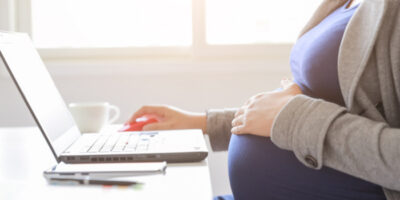 Schwangere Frau sitzt vor ihrem Laptop und arbeitet.